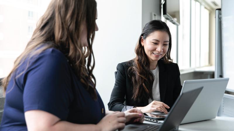 CISA employees smiling while working on laptops in a bright conference room